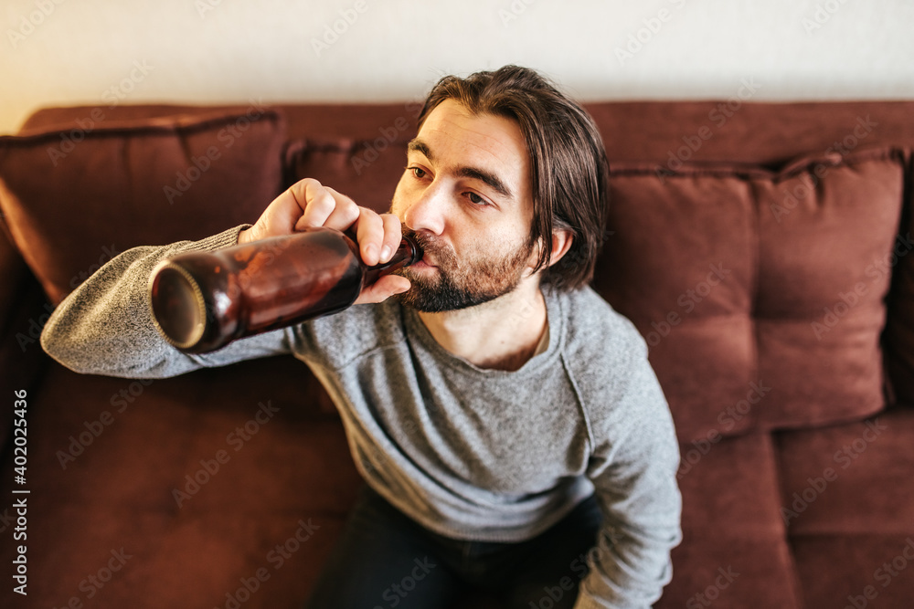 Man in his 40s at home looking at a beer bottle, thinking how to stop drinking beer every day