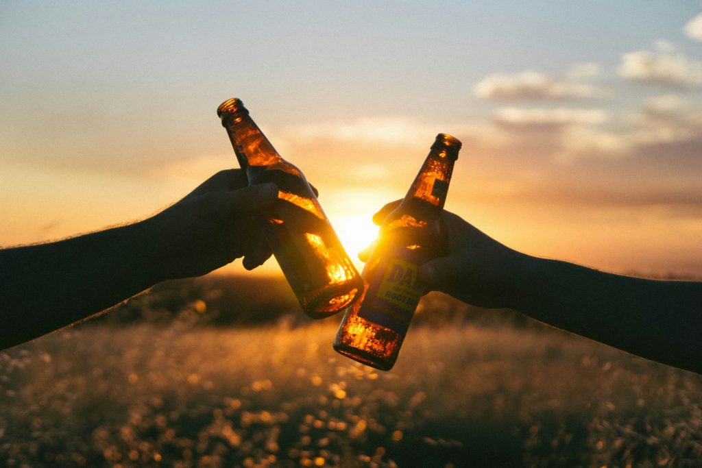 Person holding a glass bottle at sunset, symbolizing choosing sobriety instead of beer